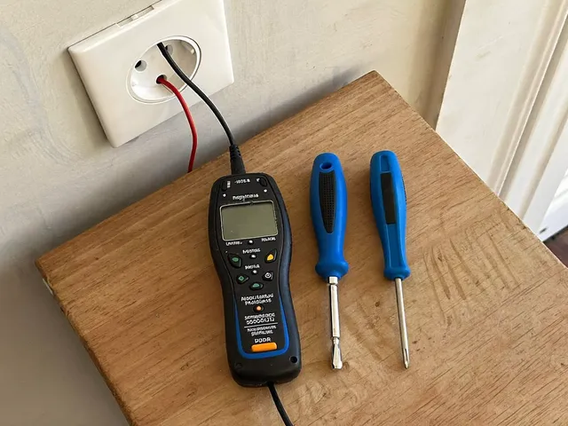 Digital multimeter and screwdrivers next to an opened wall socket